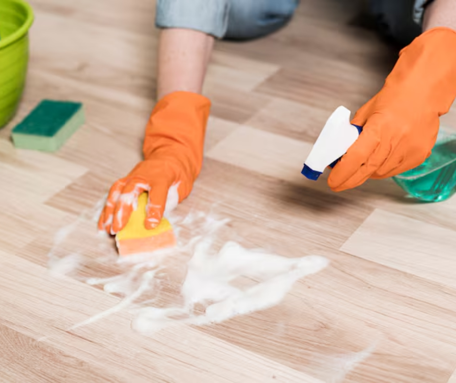 Person cleaning wooden floor with spray and sponge